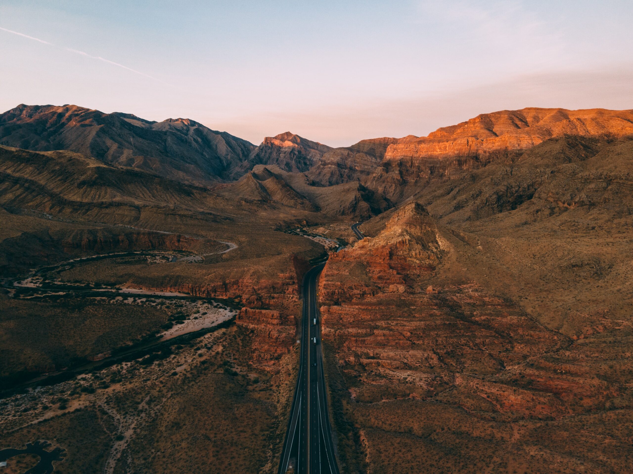 Paved road widing through a rocky desert landscape at sunset