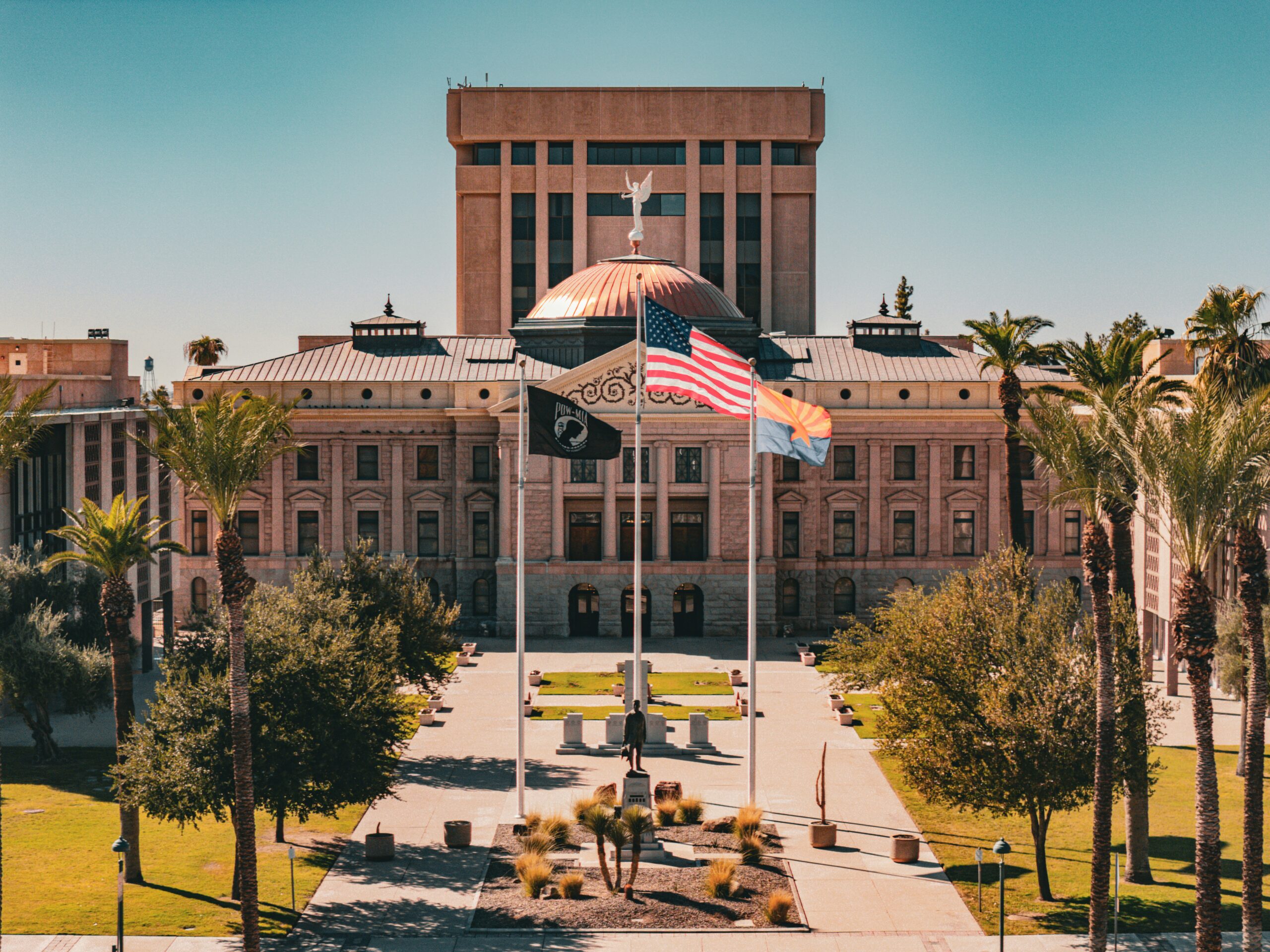 Tan capitol building with desert plants and flags flying in front of it