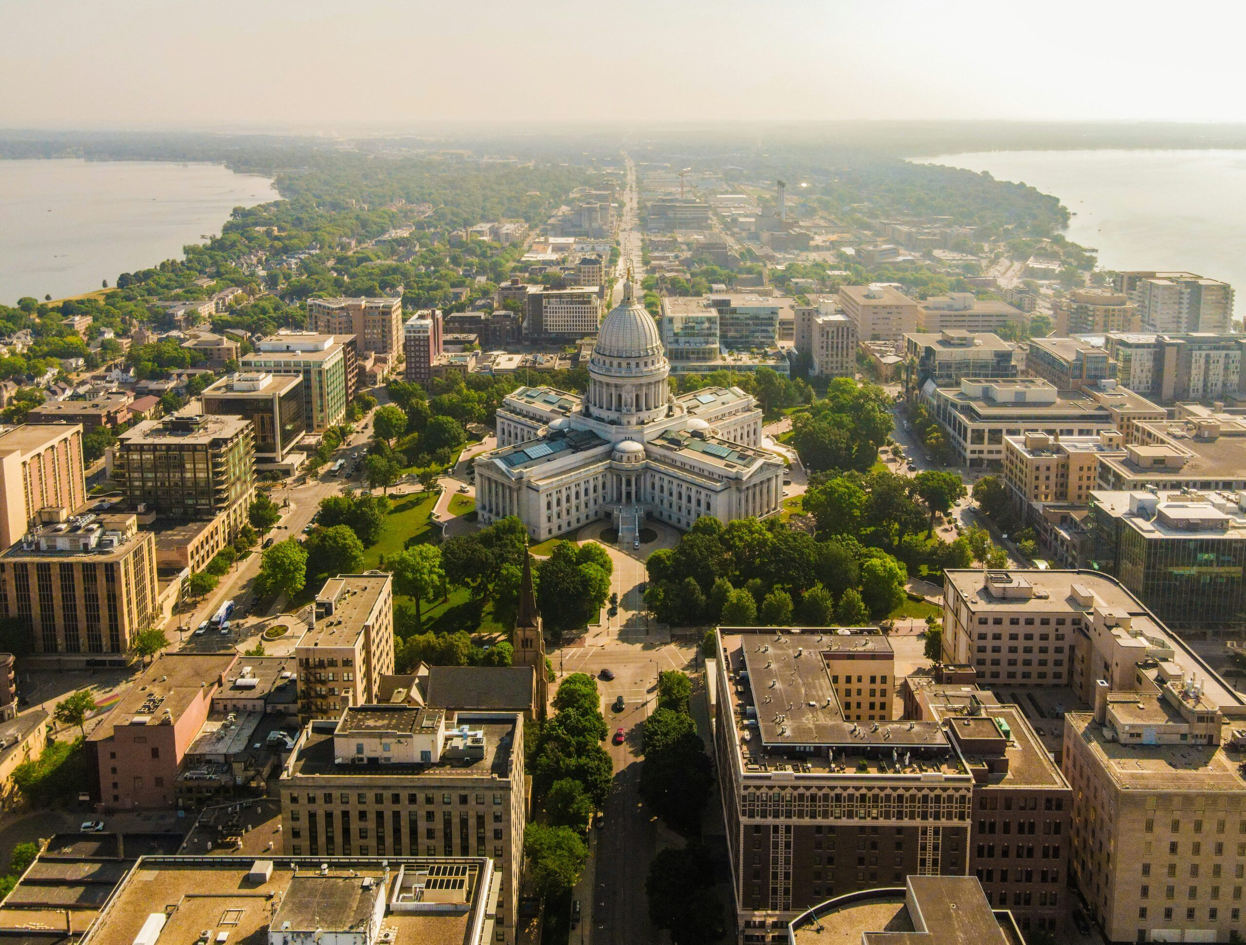 Aerial view of Wisconsin State Capitol building surrounded by vibrant green trees and city buildings