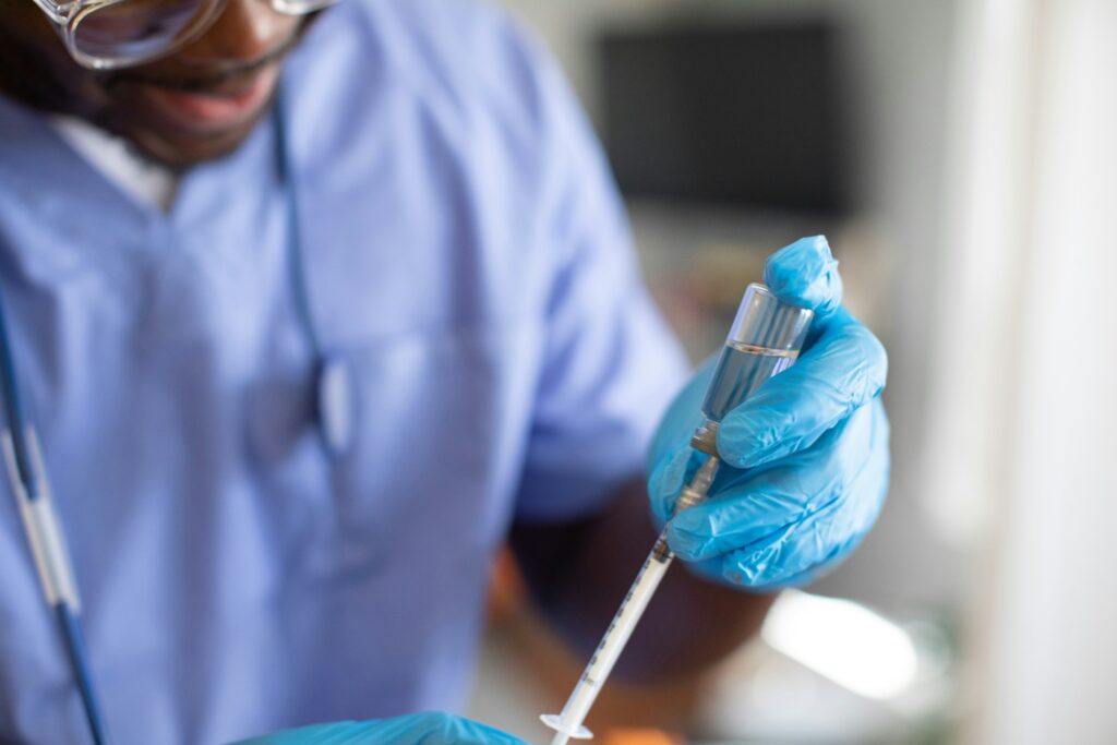 Person wearing blue scrubs and gloves holding a syringe and medicine bottle